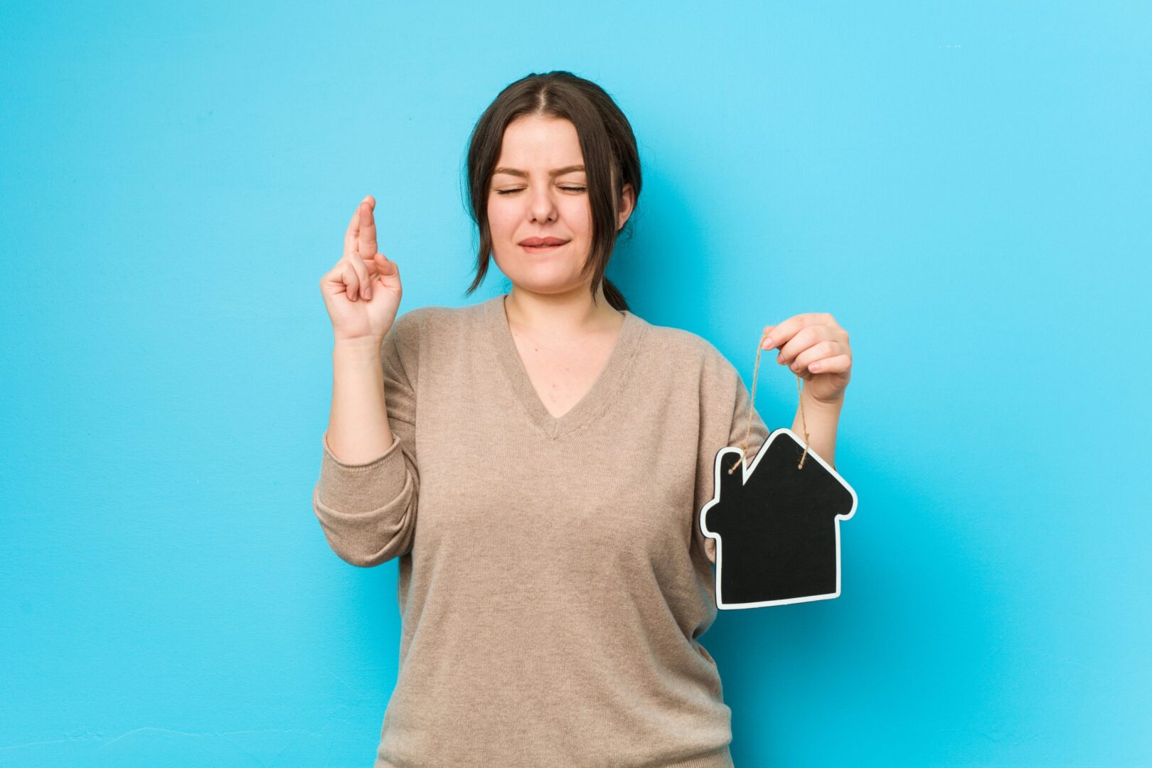 young-plus-size-curvy-woman-holding-home-icon-crossing-fingers-having-luck-scaled-1